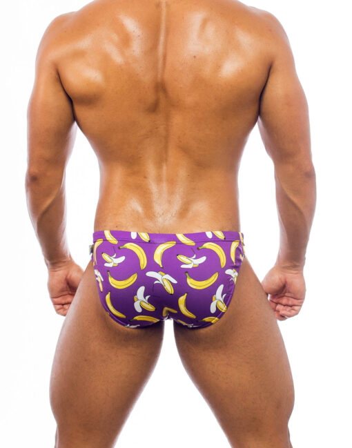 Men's swimwear, briefs style, worn by a man, rear view, pattern with a design of yellow bananas of different sizes, partially peeled, on a purple background