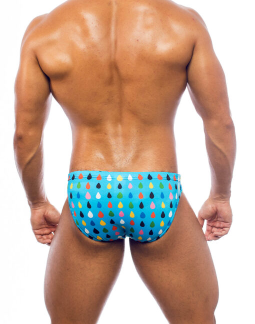 Men's swimwear, slip style, worn by a man, rear view, all-over colorful droplets pattern on a light blue background.