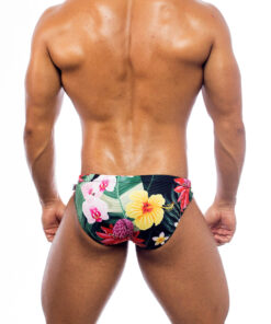 Men's swimwear, slip style, worn by a man, rear view, tropical pattern with green vegetation base and various types of pink and yellow flowers.