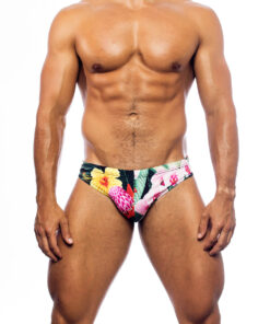 Men's swimwear, slip style, worn by a man, front view, tropical pattern with green vegetation base and various types of pink and yellow flowers.