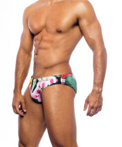 Men's swimwear, slip style, worn by a man, side view, tropical pattern with green vegetation base and various types of pink and yellow flowers.